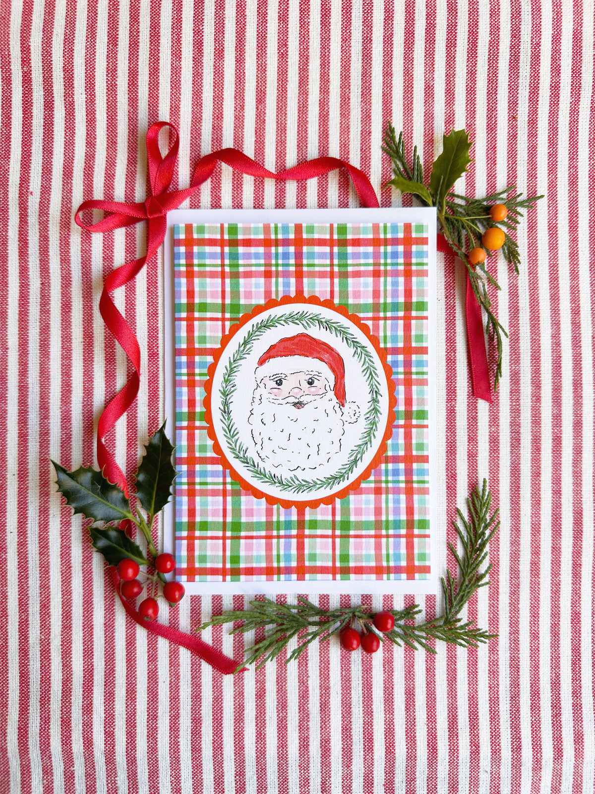 christmas card of Santa head surrounded by bows and evergreens on a red and white striped backdrop