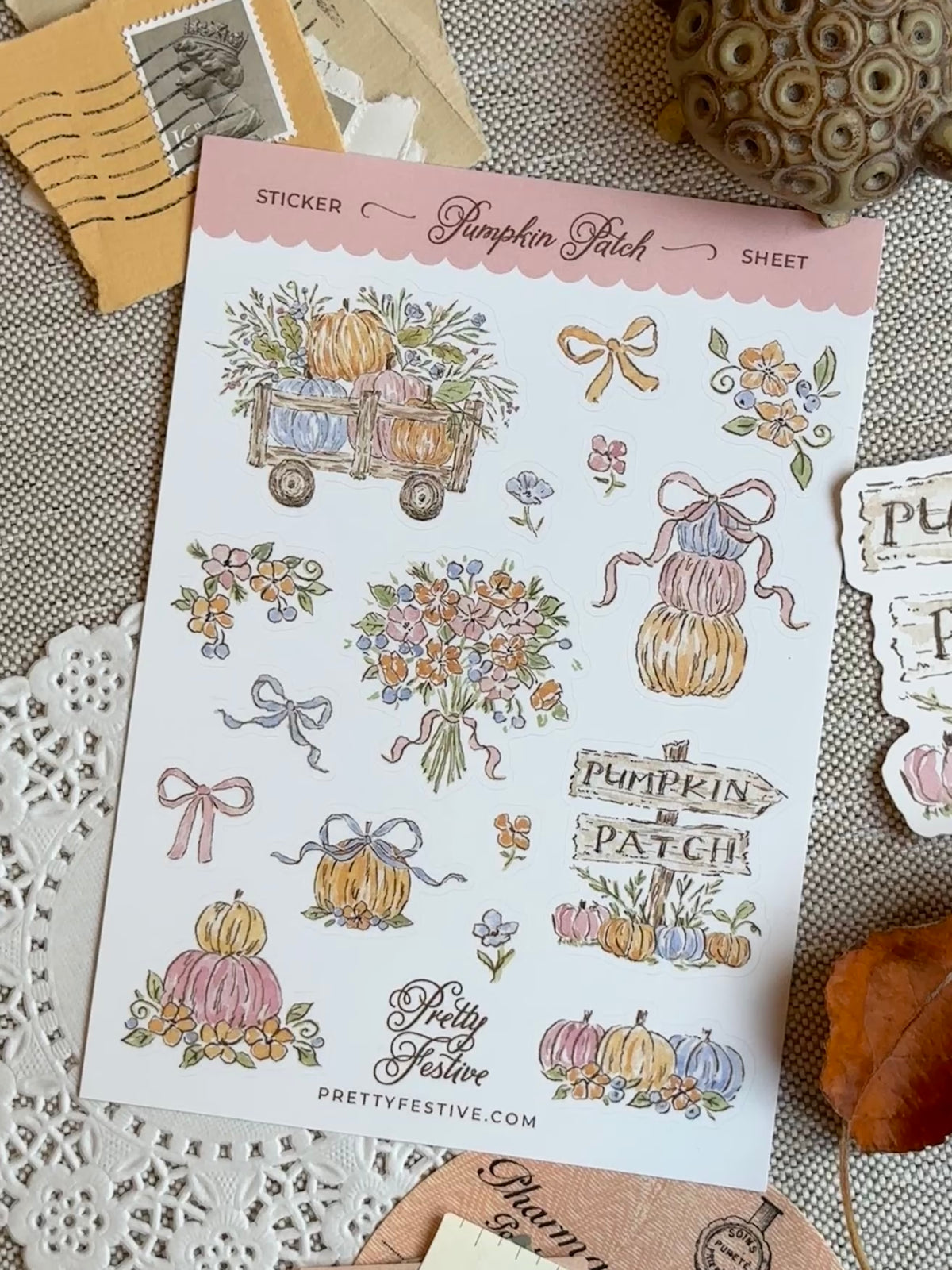 A sheet of autumn-themed stickers from Pretty Festive, featuring illustrations of pumpkins, flowers, bows, and signs like 'Pumpkin Patch' and 'Kitty Feast,' displayed on a textured fabric background with seasonal props.