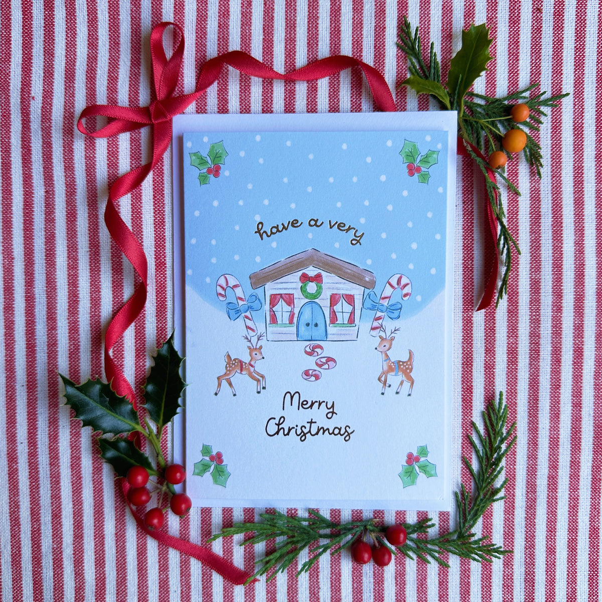 christmas card of two reindeer, a cottage and candy canes. Snow Scene. Caption have a very merry christmas. surrounded by bows and evergreens on a red and white striped backdrop