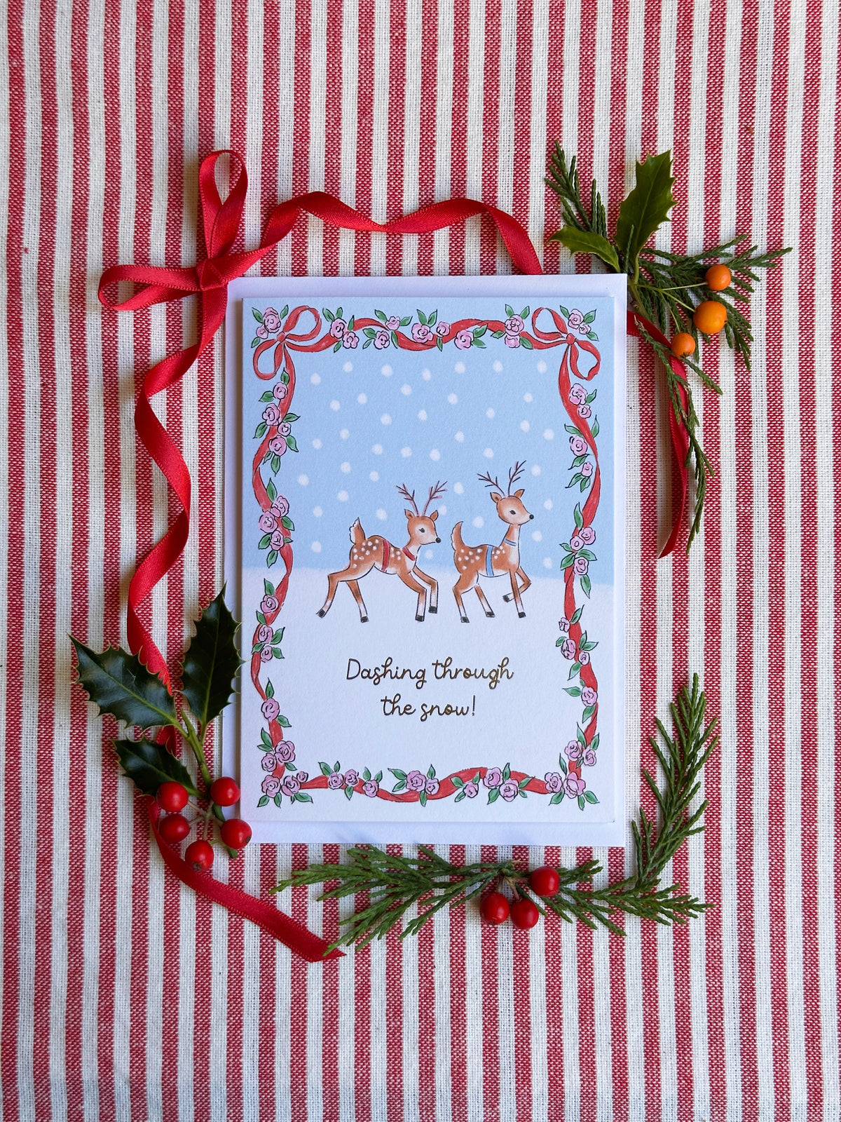christmas card of two reindeer caption Dashing Through the Snow. surrounded by bows and evergreens on a red and white striped backdrop