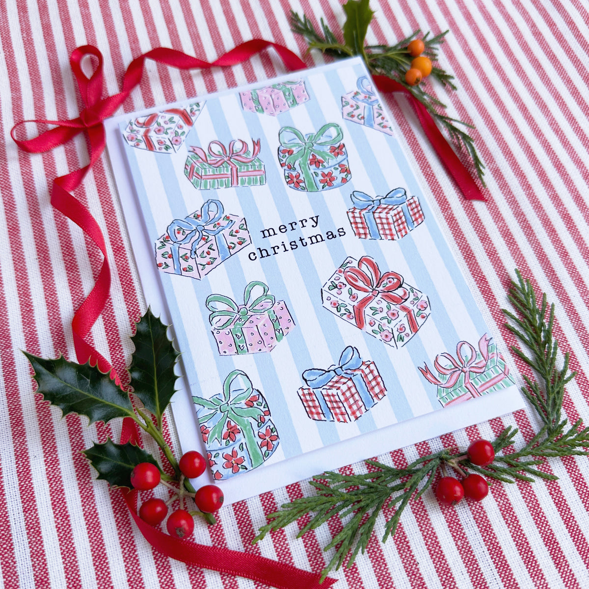 christmas card of illustrated christmas gifts surrounded by bows and evergreens on a red and white striped backdrop