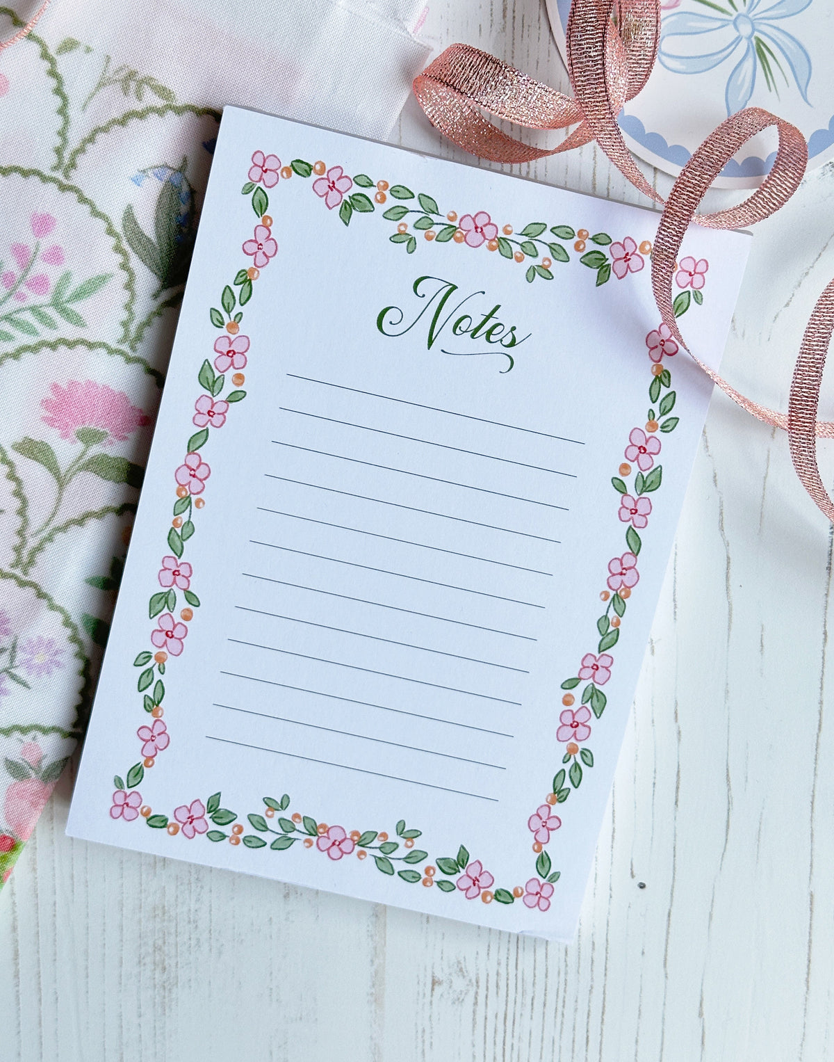 Notepad with floral border and 'Notes' text on a white surface with ribbons.