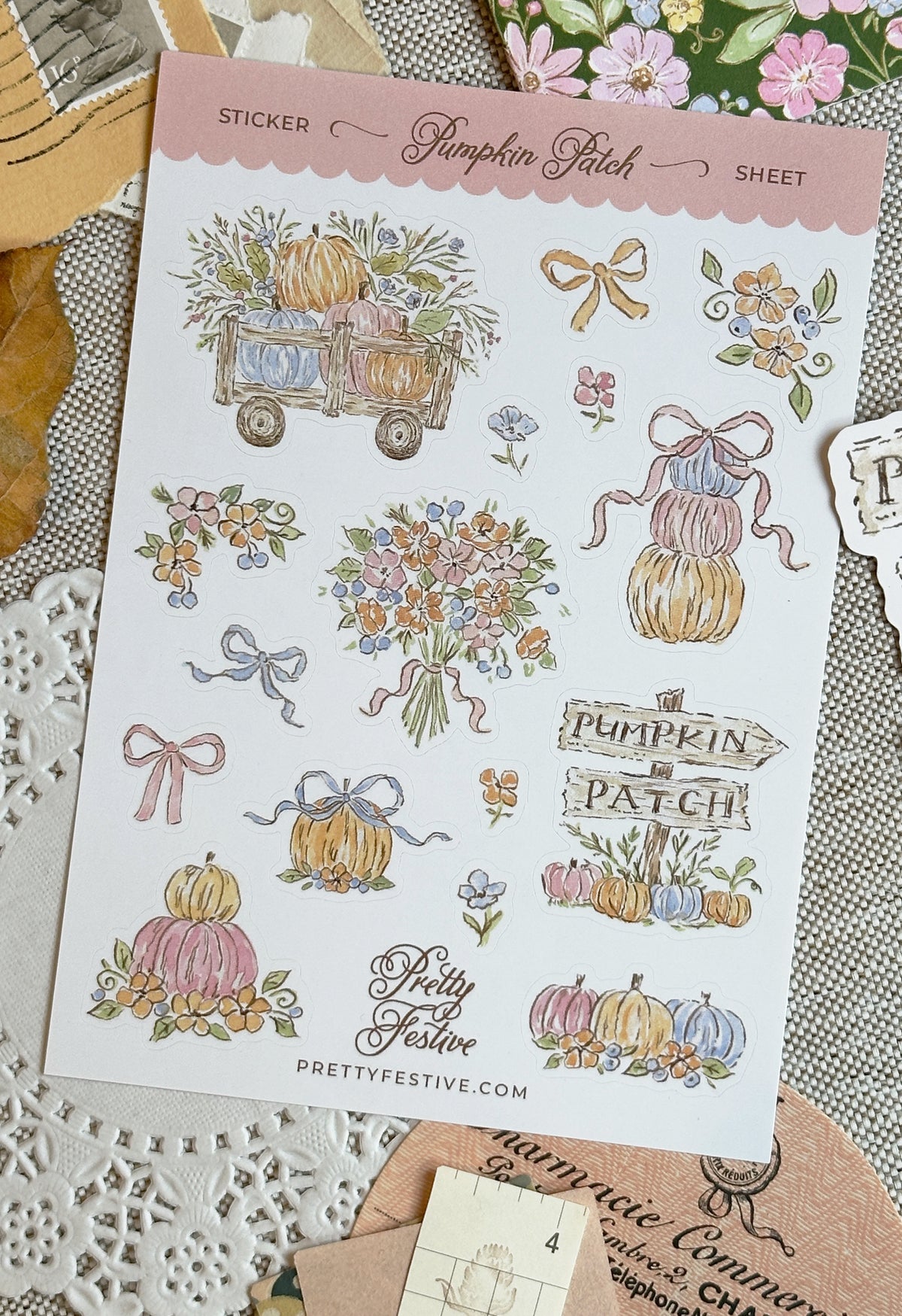 A sheet of decorative stickers labeled 'Sticker Pumpkin Patch Sheet' with multiple autumn-themed illustrations including pumpkins, flowers, bows, a wagon, and signs. The sheet is photographed on a styled flat-lay surface with lace and paper props.