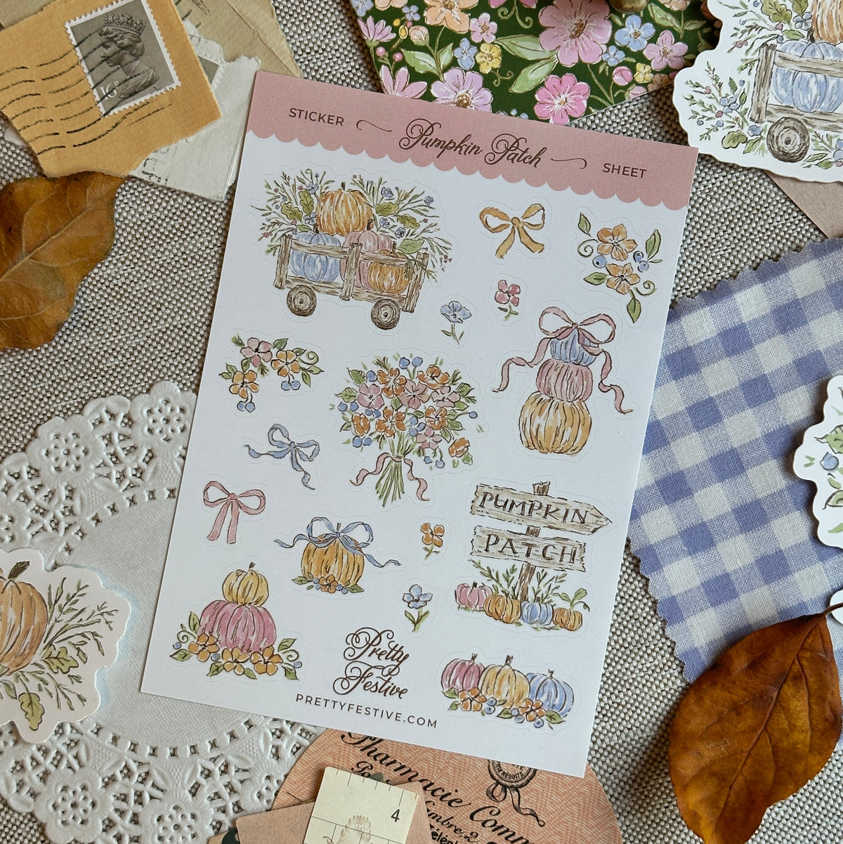 A sheet of decorative stickers featuring autumn and floral designs, including pumpkins, flowers, bows, and the text 'Pumpkin Patch' and 'Fairy Tail,' arranged on a styled flat-lay with paper doilies, leaves, and patterned cards.