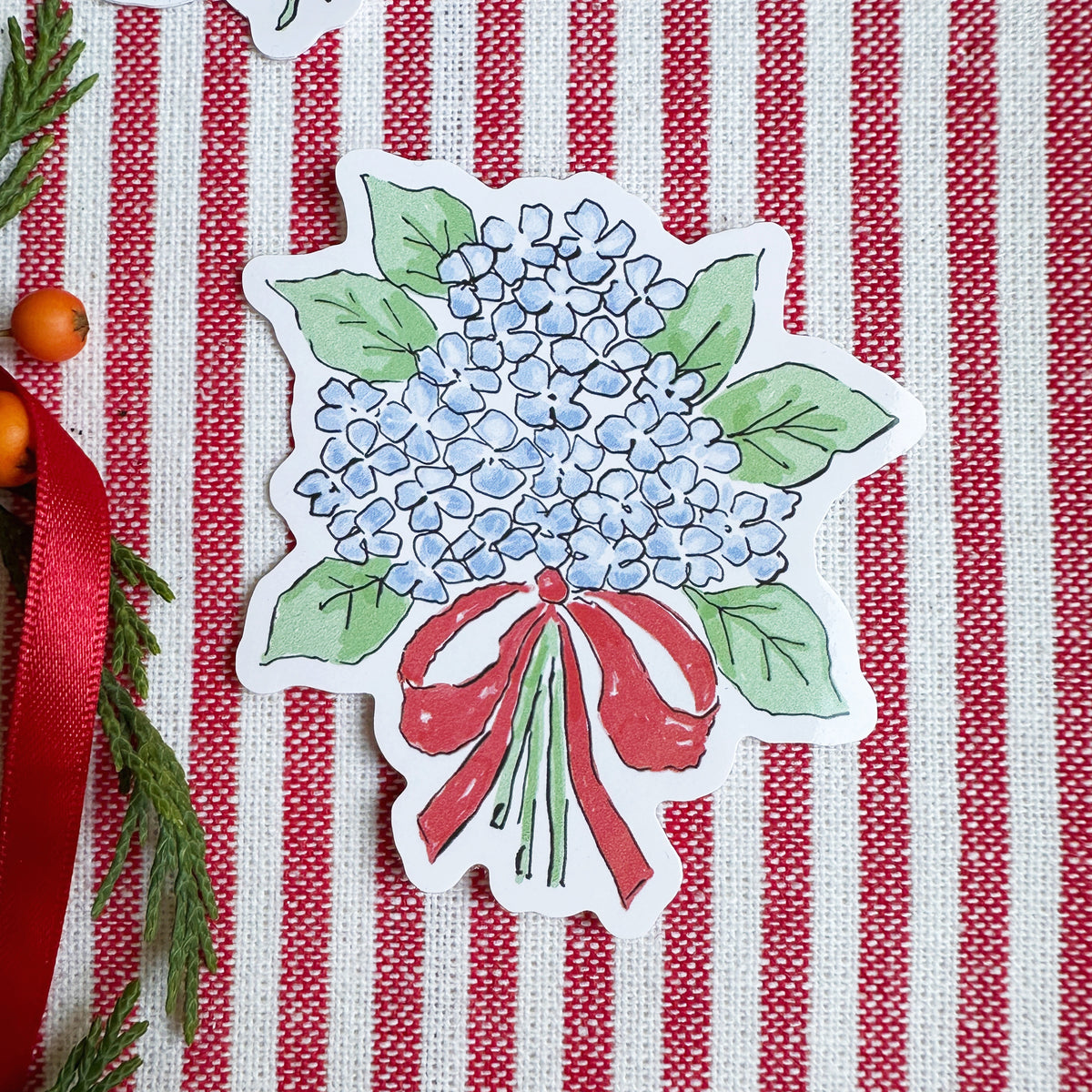 Vinyl die cut sticker of illustrated hydrangea bouquet with red bow. The background is red and white striped fabric with red ribbon greenery and berries.